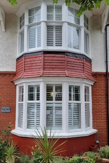 White plantation shutters cover the windows, providing privacy and style. The upper part of the bay has white framed windows traditional UK house