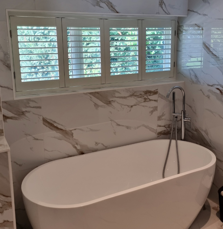 The window is adorned with sleek plantation shutters, offering a stylish and functional window treatment that complements the luxurious marble walls and creates a bright, inviting atmosphere