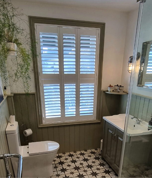 Stylish modern bathroom with plantation shutters, green panelled walls, patterned star floor tiles, wall-mounted plant, and compact vanity unit.