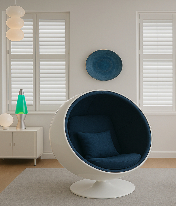 Contemporary lounge corner with white tier-on-tier plantation shutters, globe pendant light, green lava lamp and spherical table lamp on a white sideboard, round pod chair with navy cushion, and blue wall art.